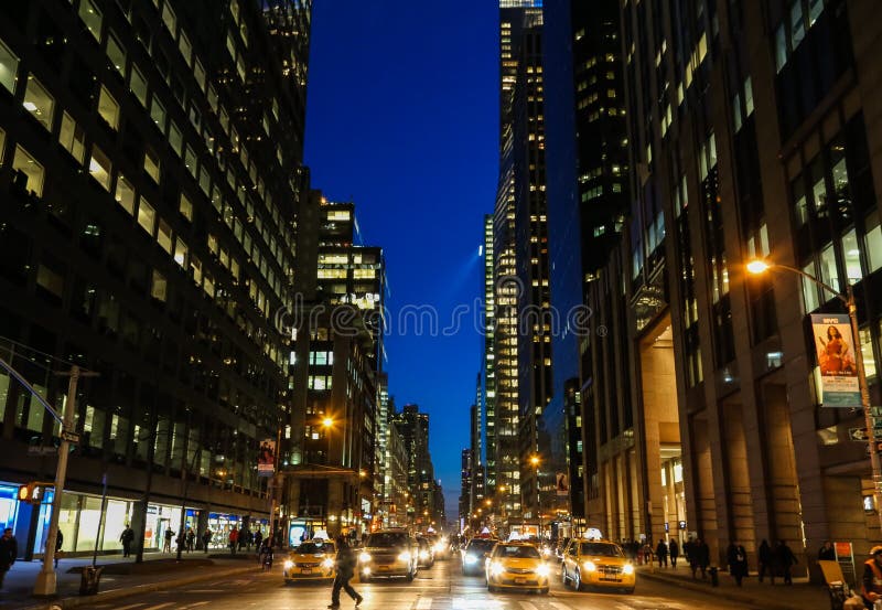 New York city street at night with a pedestrian on a crosswalk in front of yellow taxi cabs. New York city street at night with a pedestrian on a crosswalk in front of yellow taxi cabs