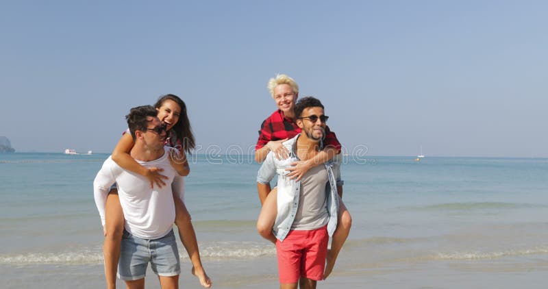Οι άνδρες φέρνουν τις γυναίκες στην πλάτη, δύο ζεύγη που περπατούν στους ευτυχείς εύθυμους ανθρώπους παραλιών που μιλούν τους του απόθεμα βίντεο