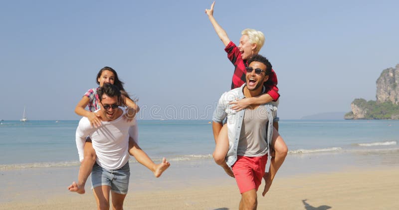 Οι άνδρες φέρνουν τις γυναίκες στην πλάτη, δύο ζεύγη που τρέχουν στους ευτυχείς εύθυμους τουρίστες ανθρώπων παραλιών στις διακοπέ απόθεμα βίντεο