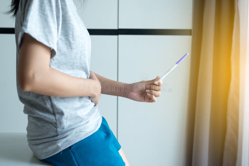 Οι ασιατικές γυναίκες δίνουν σχετικά με την κοιλιά της μετά από να εξετάσουν τη δοκιμή εγκυμοσύνης στην κρεβατοκάμαρά της, κλείνο στοκ εικόνες με δικαίωμα ελεύθερης χρήσης