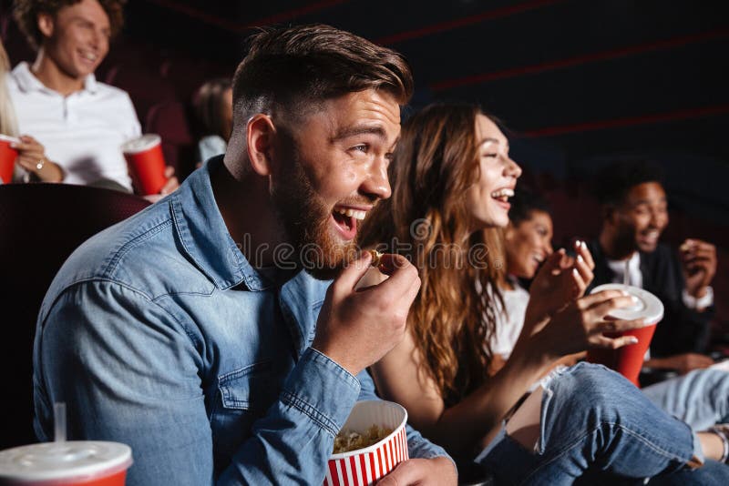 Image of laughing friends sitting in cinema watch film eating popcorn and drinking aerated sweet water. Image of laughing friends sitting in cinema watch film eating popcorn and drinking aerated sweet water.