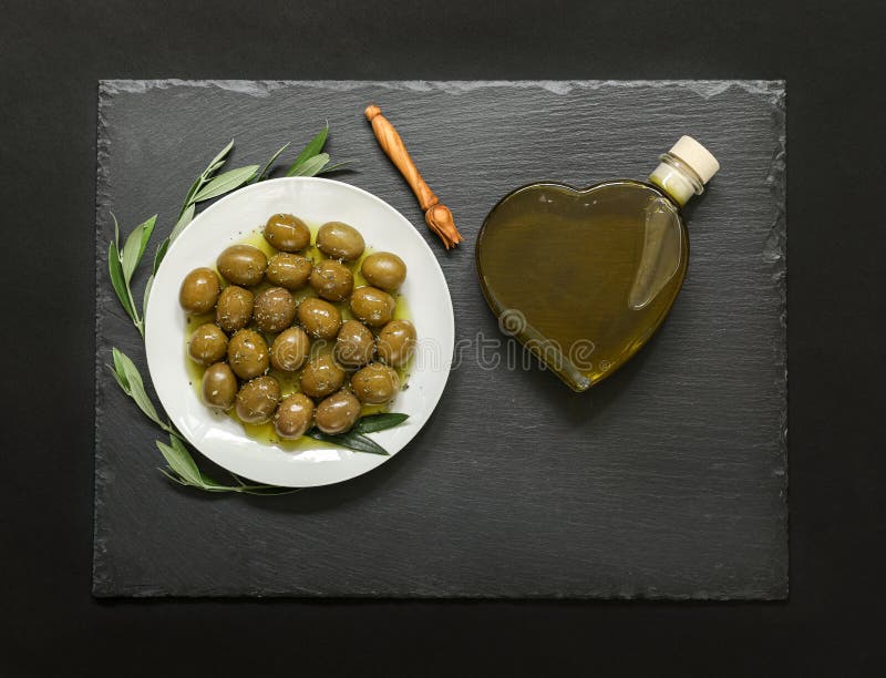 Οι επιλεγμένες ελιές σε ένα άσπρο πιάτο που διακοσμείται με τη φυσική ελιά διακλαδίζονται και το μπουκάλι καρδιών ελαιολάδου στοκ εικόνες Οι επιλεγμένες ελιές σε ένα άσπρο πιάτο που διακοσμείται με τη φυσική ελιά διακλαδίζονται και το μπουκάλι καρδιών ελαιολάδου στοκ εικόνες