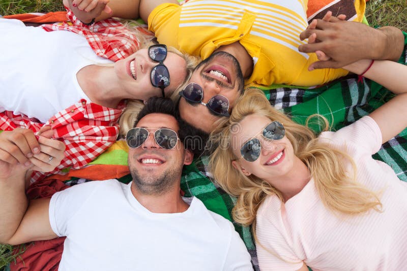 Happy people group young friends lying down on picnic blanket outdoor, two couple summer sunny day smile top angle view. Happy people group young friends lying down on picnic blanket outdoor, two couple summer sunny day smile top angle view