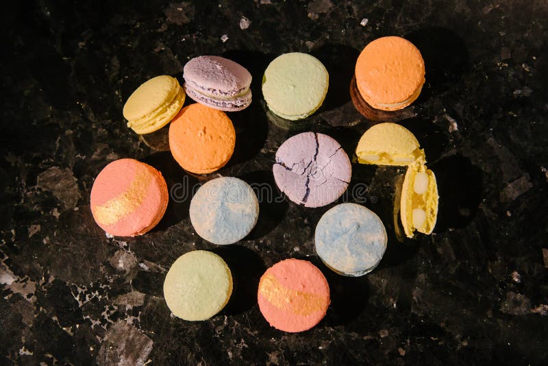 Top view of sweet and colorful desserts - macarons - laid out on a dark table. One dessert is crushed, and the second is broken into 2 parts. Top view of sweet and colorful desserts - macarons - laid out on a dark table. One dessert is crushed, and the second is broken into 2 parts
