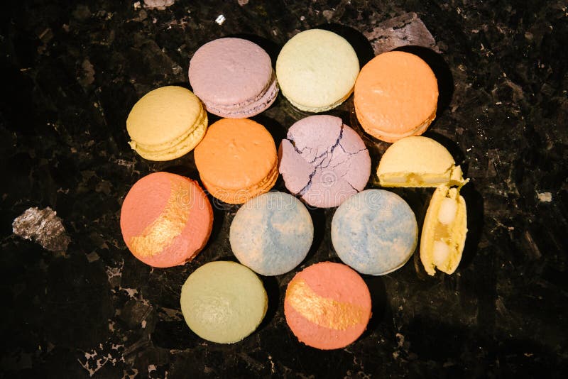 Top view of sweet and colorful desserts - macarons - laid out on a dark table. One dessert is crushed, and the second is broken into 2 parts. Top view of sweet and colorful desserts - macarons - laid out on a dark table. One dessert is crushed, and the second is broken into 2 parts