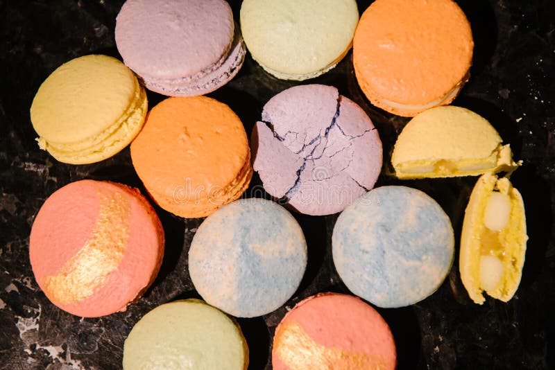 Top view of sweet and colorful desserts - macarons - laid out on a dark table. One dessert is crushed, and the second is broken into 2 parts. Top view of sweet and colorful desserts - macarons - laid out on a dark table. One dessert is crushed, and the second is broken into 2 parts