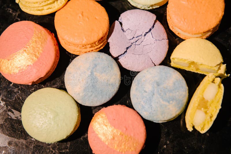 Top view of sweet and colorful desserts - macarons - laid out on a dark table. One dessert is crushed, and the second is broken into 2 parts. Top view of sweet and colorful desserts - macarons - laid out on a dark table. One dessert is crushed, and the second is broken into 2 parts