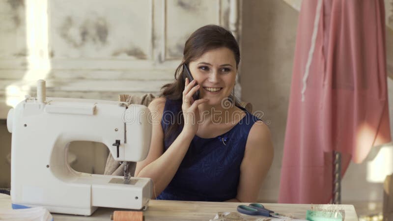 Οι νέες σχεδιαστών και seamstress ιματισμού συζητήσεις μηχανών πλησίον ραψίματος γυναικών τηλεφωνούν στο χαμόγελο στο στούντιο