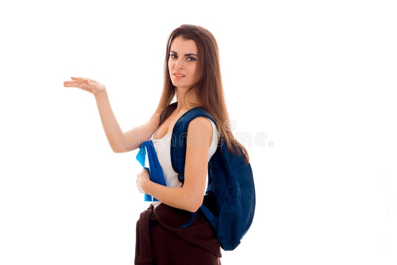 Οι νεολαίες το κορίτσι σπουδαστών brunette με το σακίδιο πλάτης στους ώμους και τα βιβλία της στα χέρια της που δείχνει την πλευρ στοκ εικόνες Οι νεολαίες το κορίτσι σπουδαστών brunette με το σακίδιο πλάτης στους ώμους και τα βιβλία της στα χέρια της που δείχνει την πλευρ στοκ εικόνες