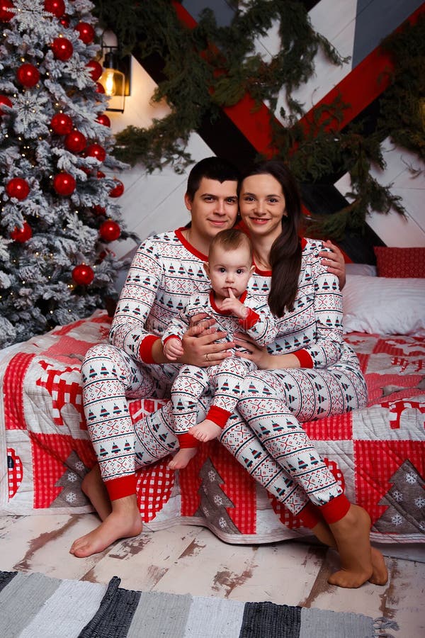 Family in pajamas sits on a bed near the Christmas tree mom, dad and toddler, idyll, Christmas celebration. family happiness. family look birth of a child for the new year family secret. Family in pajamas sits on a bed near the Christmas tree mom, dad and toddler, idyll, Christmas celebration. family happiness. family look birth of a child for the new year family secret