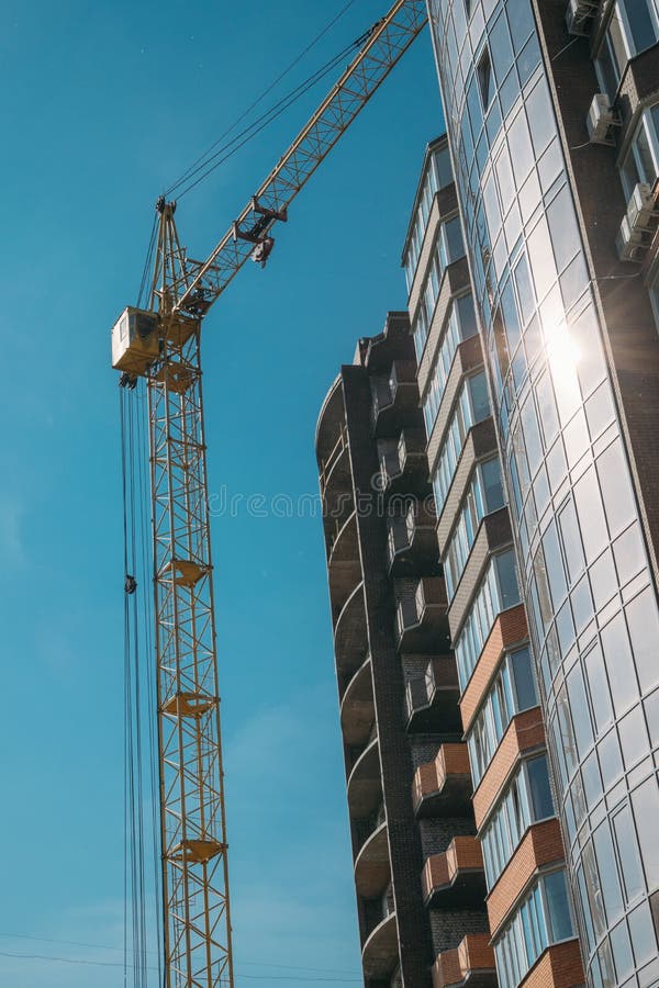 Οικοδόμηση κάτω από την κατασκευή και το γερανό κατασκευής ενάντια στο μπλε ουρανό και φωτεινός ήλιος στη θερινή ημέρα r στοκ εικόνες Οικοδόμηση κάτω από την κατασκευή και το γερανό κατασκευής ενάντια στο μπλε ουρανό και φωτεινός ήλιος στη θερινή ημέρα r στοκ εικόνες