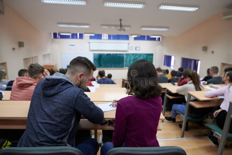 In the Classroom Multi Ethnic Students Listening to a Lecturer and Writing in Notebooks. Smart Young People Study at the College. In the Classroom Multi Ethnic Students Listening to a Lecturer and Writing in Notebooks. Smart Young People Study at the College.