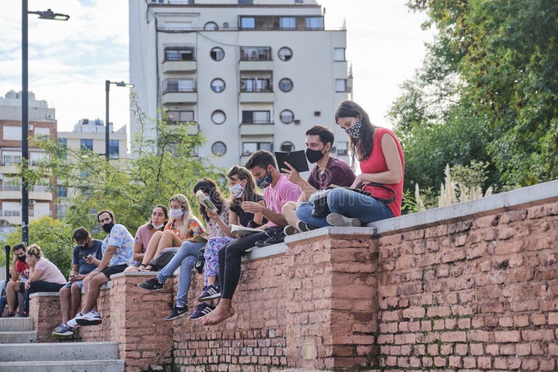 Buenos Aires, Argentina; April 2, 2021: group of young people sitting outdoors at a reading activity, using face masks for the prevention of covid, during the Felba, Publishers and Bookstores Fair. Buenos Aires, Argentina; April 2, 2021: group of young people sitting outdoors at a reading activity, using face masks for the prevention of covid, during the Felba, Publishers and Bookstores Fair