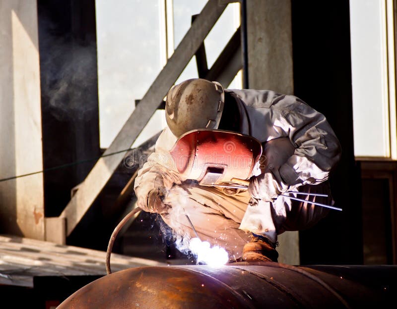 Welder welding steel in fabricating workshop. Welder welding steel in fabricating workshop.
