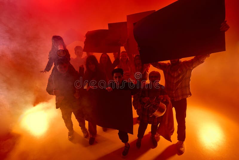 Οργισμένο πλήθος διαφορετικών ανθρώπων πορεύεται μπροστά μέσω κόκκινου νέον λάμψης κρατώντας σκοτεινά σήματα διαμαρτυρίας και φωνά στοκ φωτογραφία με δικαίωμα ελεύθερης χρήσης