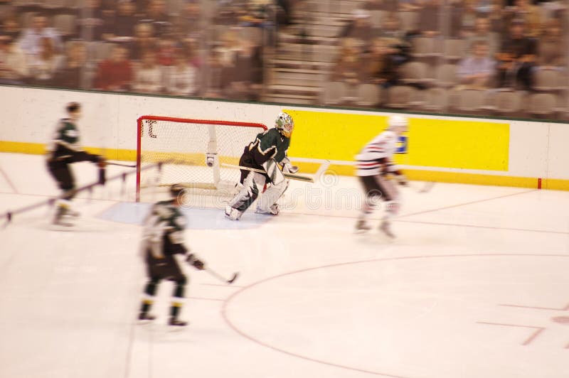 Goalie watches the puck as two man defend and one man attacks. Crowd watches in suspense. Motion blur. Goalie watches the puck as two man defend and one man attacks. Crowd watches in suspense. Motion blur.