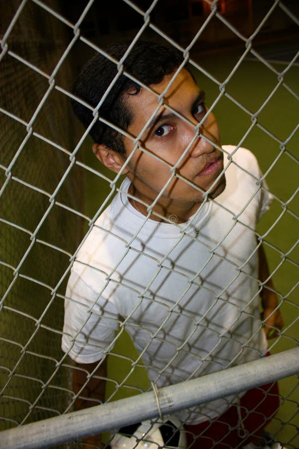 A young hispanic male looking through fence. A young hispanic male looking through fence.