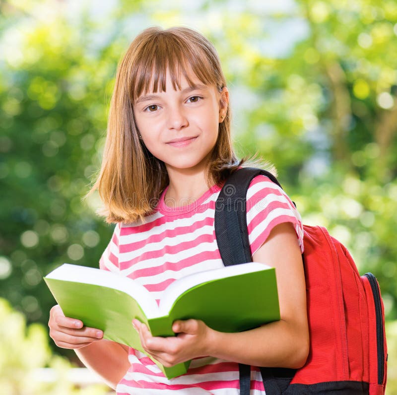 Outdoor portrait of happy girl 10-11 year old with backpack reading book. Back to school concept. Outdoor portrait of happy girl 10-11 year old with backpack reading book. Back to school concept.