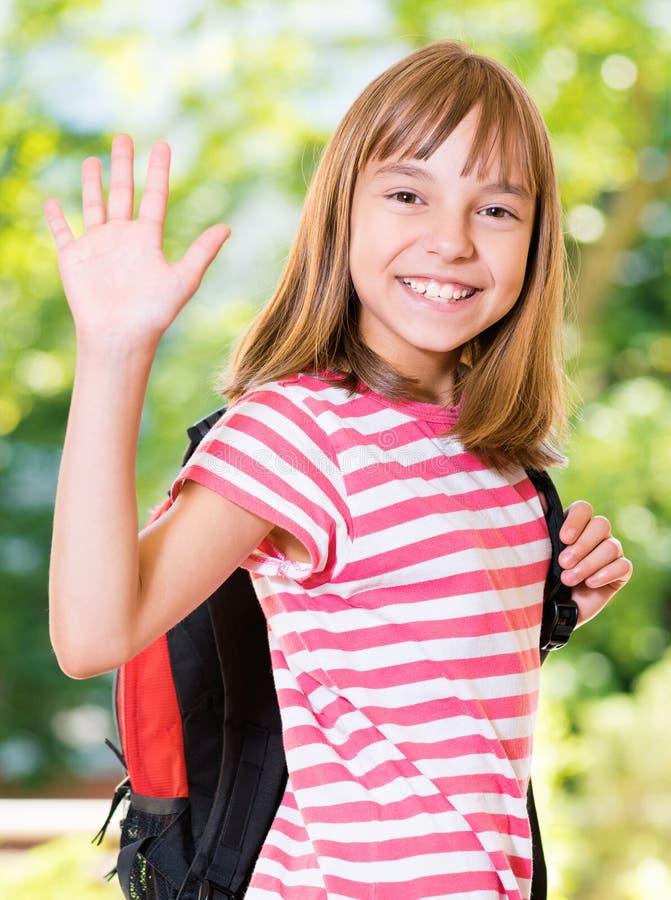 Smiling girl 10-11 year old stretching her right hand up for greeting in summer park. Beautiful schoolgirl with backpack posing outdoors. Smiling girl 10-11 year old stretching her right hand up for greeting in summer park. Beautiful schoolgirl with backpack posing outdoors.