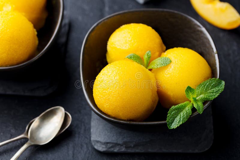 Παγωτό μάγκο και ροδάκινων, τροπικό sorbet φρούτων στο μαύρο κύπελλο στο υπόβαθρο πλακών o στοκ φωτογραφίες Παγωτό μάγκο και ροδάκινων, τροπικό sorbet φρούτων στο μαύρο κύπελλο στο υπόβαθρο πλακών o στοκ φωτογραφίες