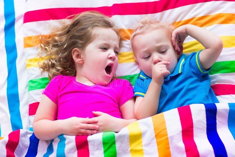 Two kids sleeping in bed under colorful blanket. Children relaxing in bedroom. Tired toddler girl and baby boy before bedtime. Rainbow textile bedding for nursery. Brother and sister play at home. Two kids sleeping in bed under colorful blanket. Children relaxing in bedroom. Tired toddler girl and baby boy before bedtime. Rainbow textile bedding for nursery. Brother and sister play at home.