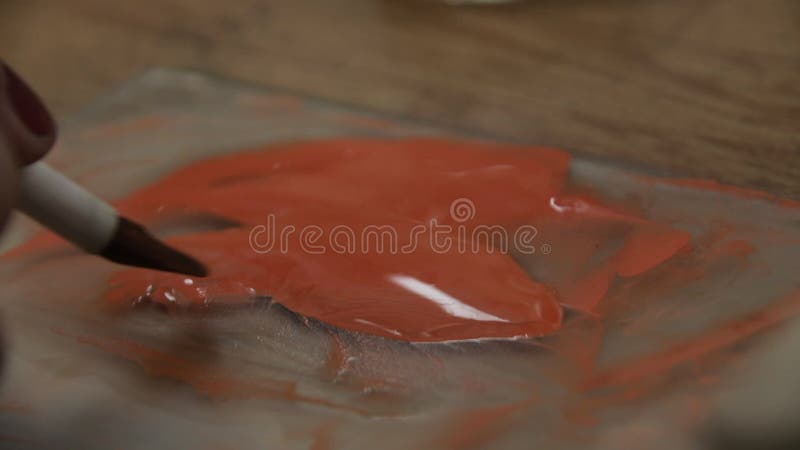 παλέτα καλλιτεχνών με πορτοκαλί χρώμα. ένα γυναικείο χέρι βουτάει στο χρώμα με ένα πινέλο.