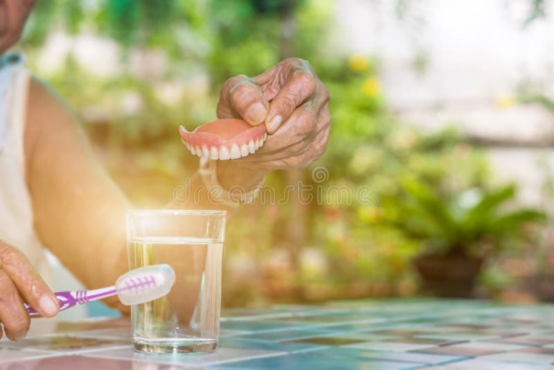 παλιές γυναίκες κρατούν ψεύτικα δόντια με βρώμικα για αποσπώμενο μερικό καθάρισμα με οδοντόβουρτσα στοκ φωτογραφίες