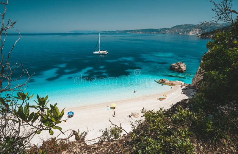 Παραλία Fteri, Cephalonia Kefalonia, Ελλάδα Άσπρο γιοτ καταμαράν στο σαφές μπλε θαλάσσιο νερό Τουρίστες στην αμμώδη παραλία πλησί στοκ φωτογραφία Παραλία Fteri, Cephalonia Kefalonia, Ελλάδα Άσπρο γιοτ καταμαράν στο σαφές μπλε θαλάσσιο νερό Τουρίστες στην αμμώδη παραλία πλησί στοκ φωτογραφία