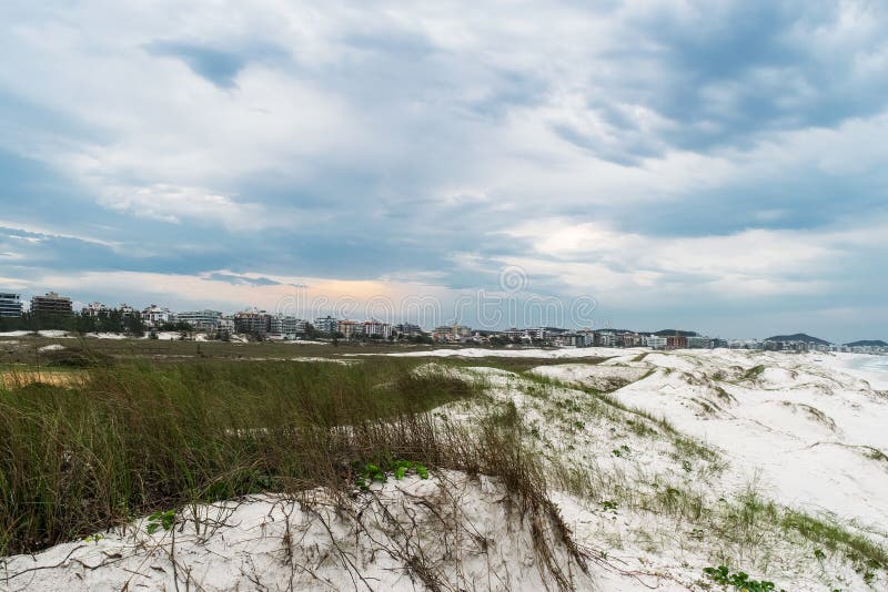 παραλία praia das dunas λευκό αμμόλοφοι θολός ουρανός και η πόλη στο φόντο. στοκ εικόνες