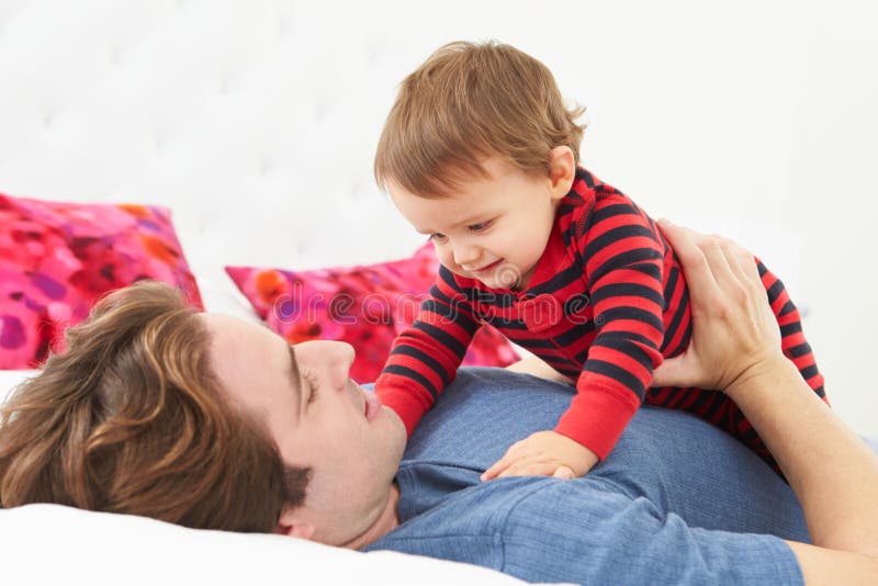 Father And Toddler Lying In Bed Together Smiling To Each Other. Father And Toddler Lying In Bed Together Smiling To Each Other