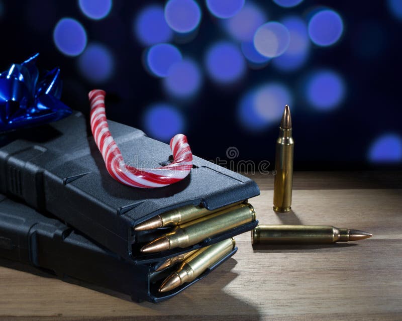 Candy cane and blue bow on top of loaded AR-15 magazines with blue holiday lights glowing behind. Candy cane and blue bow on top of loaded AR-15 magazines with blue holiday lights glowing behind