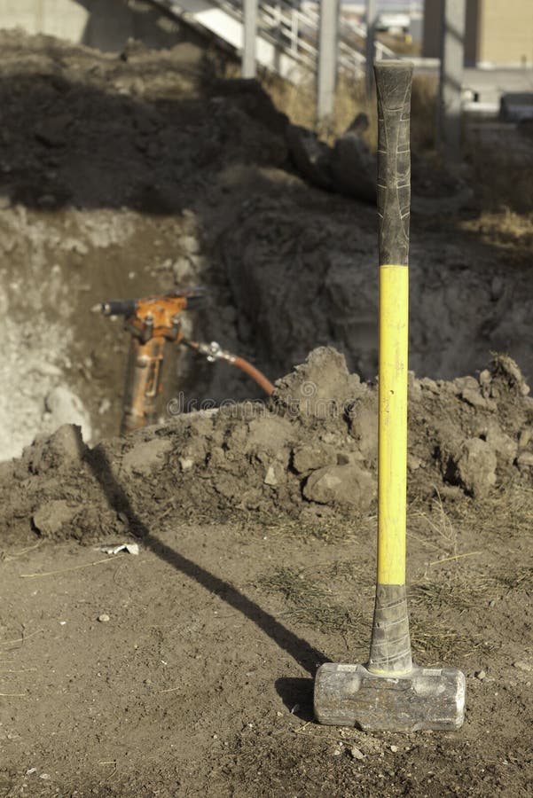 Yellow sleg hammer on construction site with a jack hammer in the background. Yellow sleg hammer on construction site with a jack hammer in the background