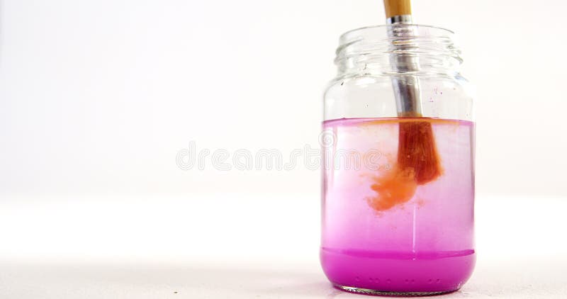 Πινέλο με την πορτοκαλιά εμβύθιση χρωμάτων στο νερό