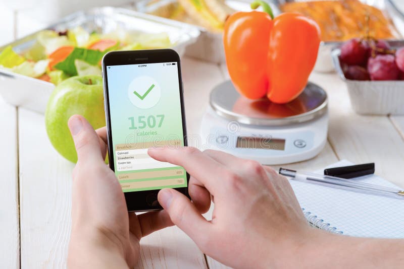 Smartphone with a calorie counter app, close-up. Paper notebook, a food scale, a pepper, an apple, salad, grapes and a pie on the background. Dieting,. Smartphone with a calorie counter app, close-up. Paper notebook, a food scale, a pepper, an apple, salad, grapes and a pie on the background. Dieting,