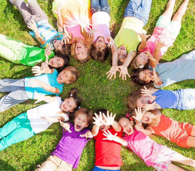 14 kids laying in a circle in the grass with happy faces shoot from above lifting hands above. 14 kids laying in a circle in the grass with happy faces shoot from above lifting hands above