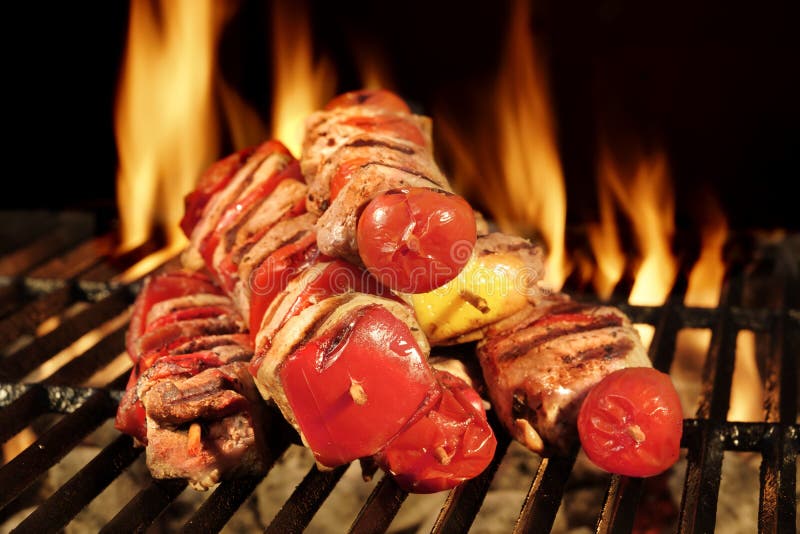 Many Shish Kebab From Different Meat With Pepper And Tomato On The Hot Charcoal BBQ Grill With Bright Flames On The Black Background, Cookout Concept, Close Up, Top View. Many Shish Kebab From Different Meat With Pepper And Tomato On The Hot Charcoal BBQ Grill With Bright Flames On The Black Background, Cookout Concept, Close Up, Top View