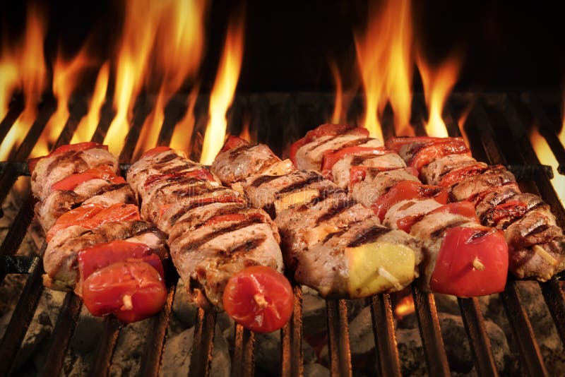 Many Shish Kebab From Different Meat With Pepper And Tomato On The Hot Charcoal BBQ Grill With Bright Flames On The Black Background, Cookout Concept, Close Up, Top View. Many Shish Kebab From Different Meat With Pepper And Tomato On The Hot Charcoal BBQ Grill With Bright Flames On The Black Background, Cookout Concept, Close Up, Top View