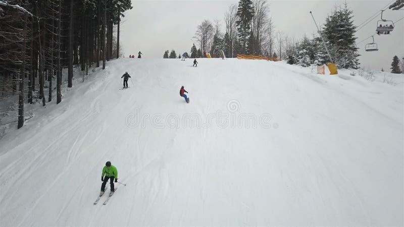 Πολλοί σκιέρ και snowboarders κατεβαίνουν κάτω από τη βουνοπλαγιά