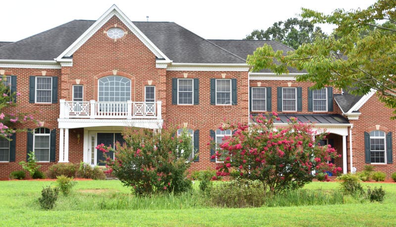 Large luxury home in a residential development. It has white columns, dark blue shutters, brick exterior, crape myrtles, and a rain garden in the front yard to collect rain water and manage stormwater runoff. Large luxury home in a residential development. It has white columns, dark blue shutters, brick exterior, crape myrtles, and a rain garden in the front yard to collect rain water and manage stormwater runoff.