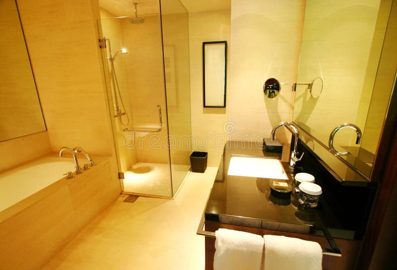 An image of a modern upscale bathroom interior in a new luxurious resort hotel and spa. Fitted with separate shower area with two different shower heads, as well as large marble bath tub, large mirrors on walls, shaving mirror, black marbletop sink and faucets area. White marble flooring. Warm lighting. Exclusive image, Horizontal color photo format, taken with wide angle lens, nobody in picture. An image of a modern upscale bathroom interior in a new luxurious resort hotel and spa. Fitted with separate shower area with two different shower heads, as well as large marble bath tub, large mirrors on walls, shaving mirror, black marbletop sink and faucets area. White marble flooring. Warm lighting. Exclusive image, Horizontal color photo format, taken with wide angle lens, nobody in picture.