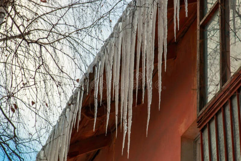 Πολύ μακριά παγάκια που κρεμούν από τη στέγη πλακών επάνω από το παράθυρο σε ένα κλίμα των άσπρων σύννεφων στοκ φωτογραφία με δικαίωμα ελεύθερης χρήσης Πολύ μακριά παγάκια που κρεμούν από τη στέγη πλακών επάνω από το παράθυρο σε ένα κλίμα των άσπρων σύννεφων στοκ φωτογραφία με δικαίωμα ελεύθερης χρήσης