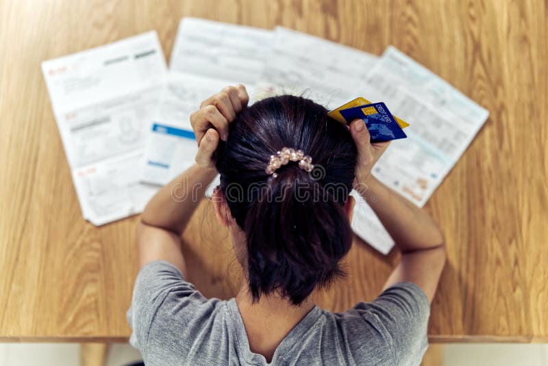 Top view of stressed young sitting Asian woman hands holding the head worry about find money to pay credit card debt and all loan bills. Financial problem concept. Top view of stressed young sitting Asian woman hands holding the head worry about find money to pay credit card debt and all loan bills. Financial problem concept.
