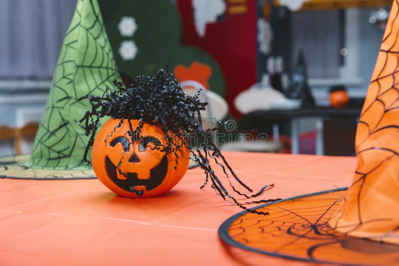 1 orange pumpkin, green and yellow witch hats on the table. 1 orange pumpkin, green and yellow witch hats on the table