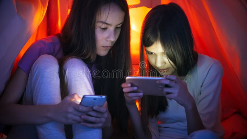 Πορτρέτο δύο έφηβη με τα έξυπνα τηλέφωνα κάτω από το κάλυμμα τη νύχτα στοκ φωτογραφία Πορτρέτο δύο έφηβη με τα έξυπνα τηλέφωνα κάτω από το κάλυμμα τη νύχτα στοκ φωτογραφία