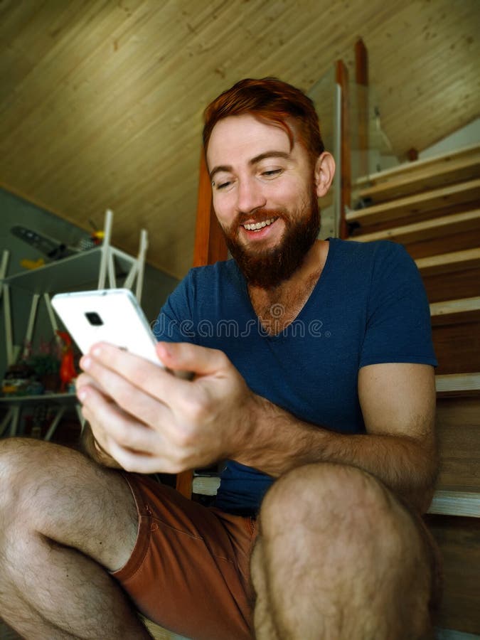 Πορτρέτο ενός νέου όμορφου redhead ατόμου με μια γενειάδα που χαλαρώνει στο σπίτι να χρησιμοποιήσει με κινητό τηλέφωνο στοκ φωτογραφίες με δικαίωμα ελεύθερης χρήσης Πορτρέτο ενός νέου όμορφου redhead ατόμου με μια γενειάδα που χαλαρώνει στο σπίτι να χρησιμοποιήσει με κινητό τηλέφωνο στοκ φωτογραφίες με δικαίωμα ελεύθερης χρήσης