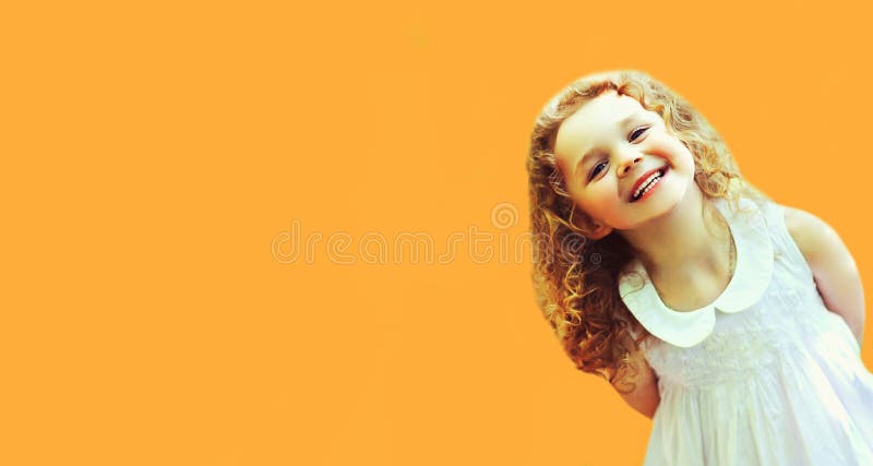 πορτρέτο ενός χαρούμενου γελαστού μικρού κοριτσιού με λευκό φόρεμα σε πορτοκαλί φόντο κενό για διαφημιστικό κείμενο