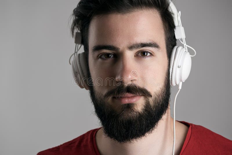 Πορτρέτο κινηματογραφήσεων σε πρώτο πλάνο του νέου γενειοφόρου ατόμου με τα ακουστικά που ακούει τη μουσική στοκ εικόνες Πορτρέτο κινηματογραφήσεων σε πρώτο πλάνο του νέου γενειοφόρου ατόμου με τα ακουστικά που ακούει τη μουσική στοκ εικόνες