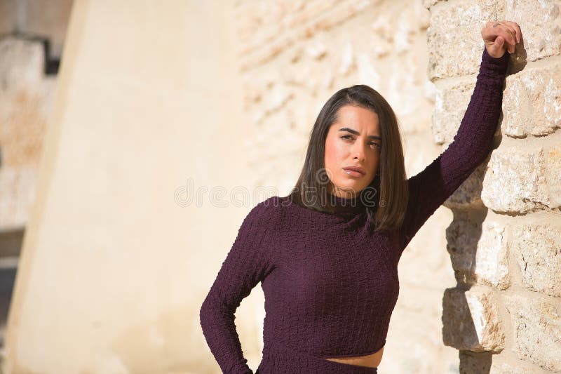 Πορτρέτο μιας νεαρής όμορφης μελαχρινής γυναίκας με ένα μωβ φόρεμα να ακουμπά σε έναν τοίχο κοιτώντας την κάμερα με μια στοκ εικόνες με δικαίωμα ελεύθερης χρήσης