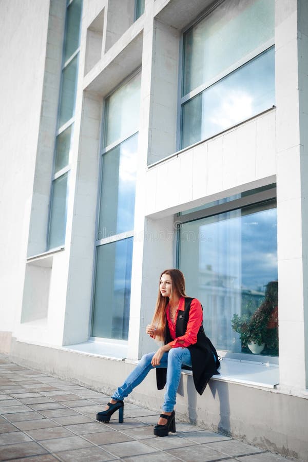 Πορτρέτο της νέας κυρίας σε ένα κόκκινο πουκάμισο και μια μακροχρόνια αμάνικη συνεδρίαση σακακιών μπροστά από τις αντανακλημένες στοκ εικόνες με δικαίωμα ελεύθερης χρήσης Πορτρέτο της νέας κυρίας σε ένα κόκκινο πουκάμισο και μια μακροχρόνια αμάνικη συνεδρίαση σακακιών μπροστά από τις αντανακλημένες στοκ εικόνες με δικαίωμα ελεύθερης χρήσης