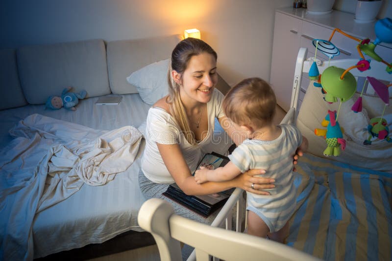 Πορτρέτο της όμορφης μητέρας που παίρνει το μωρό από το παχνί τη νύχτα στοκ φωτογραφία με δικαίωμα ελεύθερης χρήσης Πορτρέτο της όμορφης μητέρας που παίρνει το μωρό από το παχνί τη νύχτα στοκ φωτογραφία με δικαίωμα ελεύθερης χρήσης